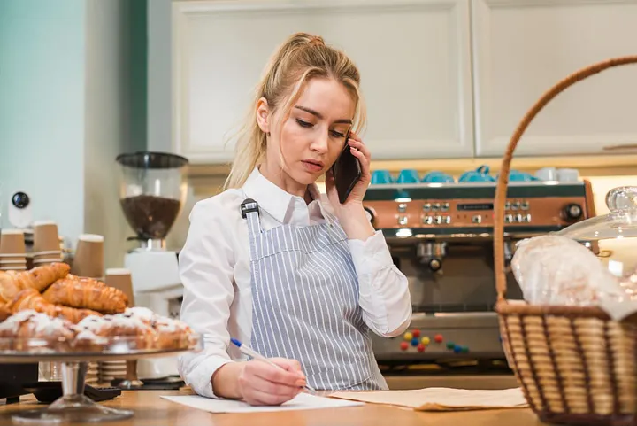 A young person calculating bakery profit margin, calculating cost and earnings while talking on the phone